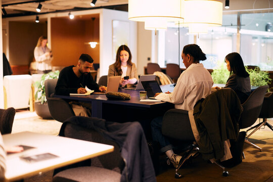 Male and female business professionals working on laptop in open plan illuminated office