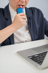 Business woman smoking an electronic cigarette while working on a laptop. Tobacco heating system.