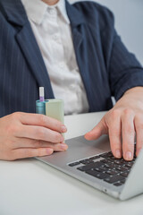 Business woman smoking an electronic cigarette while working on a laptop. Tobacco heating system. 