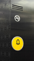 Yellow emergency elevator button, tactile braille design, urban navigation, accessibility awareness, No Smoking Day, unexpected urban intimacy