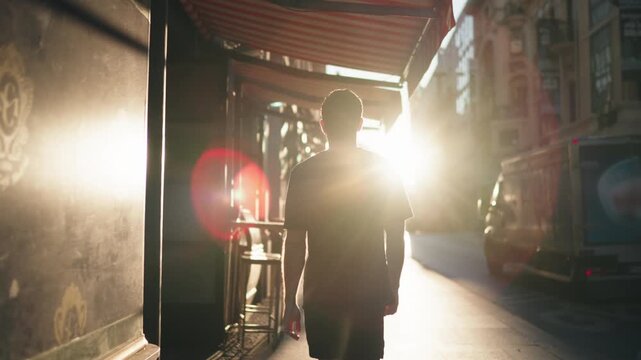 Rear view of man walking in city street at sunrise, sunlight illuminating path. Represents freedom, reflection, and balance in active urban lifestyle
