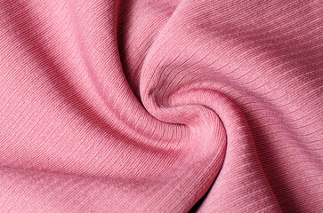 Delicate light pink fabric twisted into spiral shape creating soft textile background for fashion design and elegant decorative concepts