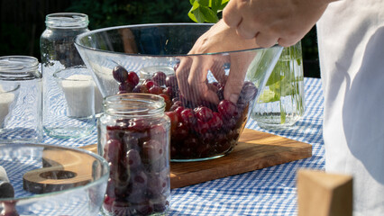 White apron-clad hand swirls ripe cherries in glass bowl, echoing Sukkot harvest rhythms amidst gingham-clad summertime brunch