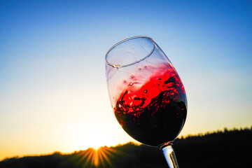 Red wine swirling on blue sky. Sommelier swirls with glass of red wine at sunset sky. Red Wine...