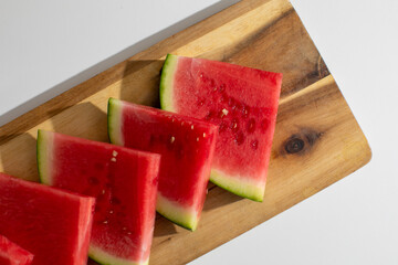 Slices of vibrant watermelon bask in sunlight on rustic board, hinting at a Festivus feast and summer solstice