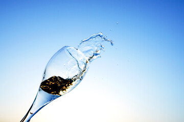 Champagne splashes from champagne glass on sunset blue sky. Romantic glass of white wine with...