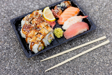 A variety of sushi including eel and salmon with garnishes of lemon and wasabi placed on a textured surface with chopsticks nearby for easy eating