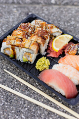 A colorful assortment of sushi and sashimi displayed on a black tray, featuring eel rolls and fresh slices of tuna, salmon, and shrimp, accompanied by wasabi and lemon