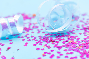 Scattered pink heart-shaped confetti and shiny white curled ribbon on a light blue background,...