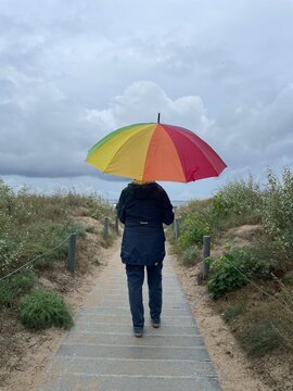 Woman with an open rainbow umbrella on a rainy day walking a beach access to the  Baltic Sea on the island Usedom, Mecklenburg Vorpommern, Germany, Europe 