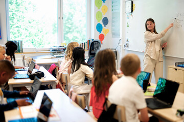 Female teacher explaining students over whiteboard at elementary school