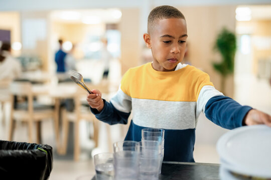 Boy stacking plate after eating meal during lunch break in school cafeteria