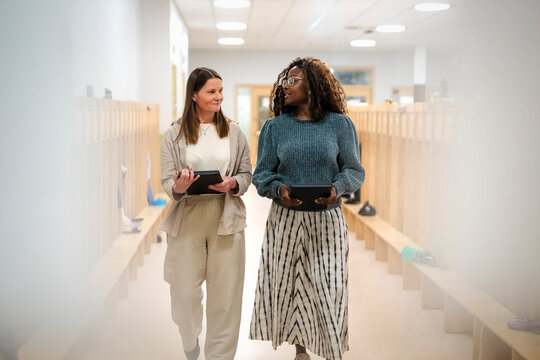 Multiracial female teachers talking with each other while walking in corridor at elementary school