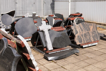 Gravestones are organized in a stoneworks yard under clear skies, showcasing a variety of shapes...