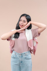 Asian woman posing with charming smile and playful hand gesture, wearing pastel casual outfit with jeans and sweater, showing cheerful expression and modern lifestyle fashion.