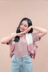 Asian woman in casual modern outfit posing with closed eyes and smiling expression, wearing pink shirt and jeans, showing relaxed and cheerful mood.