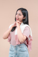 Asian woman in casual modern fashion smiling with hands under chin, wearing pink shirt and denim jeans, looking cheerful and expressive with a positive lifestyle vibe.