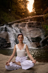 Young woman sitting in lotus pose under tropical waterfall meditating with calm strength and mindfulness fully connected to nature energy tranquility and inner balance