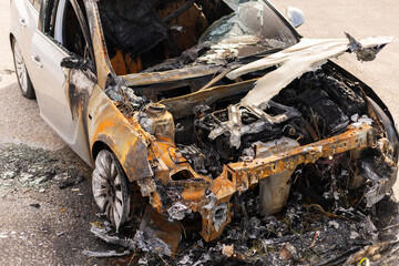Fototapeta premium A burned car sits abandoned with charred remains and melted components. The wreckage displays extensive heat damage, revealing the engine and interior