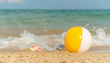 Obraz premium Yellow and white beach ball on a sandy shore with gentle ocean waves.