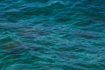 Obraz premium Sea surface aerial view. Background shot of clear sea water surface. Blue sea water in calm. Sea texture. Background blue waves of the sea with sea foam. 