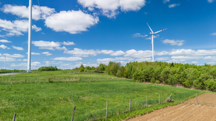 Fototapeta premium Aerial view of lush green fields with electricity wind turbines on a sunny day. The scene captures renewable energy in a serene rural landscape, highlighting nature's balance.