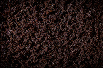 Texture of smoothed wet coffee grounds. Small brown crumbs with lumps form a smooth, textured surface. Close-up.