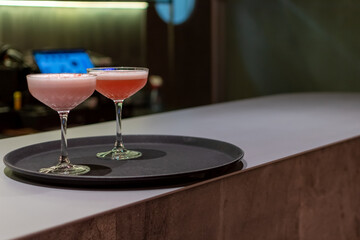 Elegant cocktails in coupe glasses on bar on a serving tray