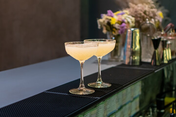 Two elegant glasses and the final finished beverages waiting on the bar. Other bar tools and...