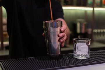 Bartender in a black shirt is carefully pouring a red liquid from a bottle into a metal jigger
