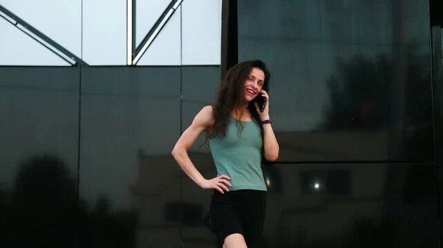 Young fit sporty woman in the city talking on mobile phone near office building in summer day with happy smiling - Powered by Adobe