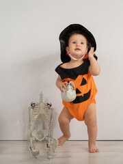 Cute caucasian boy in pumpkin costume for halloween holding skull on white background. 