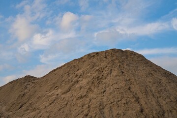 A large pile of soil against a blue sky with clouds. Earth mound from construction or landscaping work.