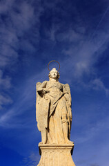 Obraz premium Historic statue of the Archangel Raphael, patron saint of Cordoba. It is located on the Roman Bridge which spans the Gaudalquivir River. Backed by Cirrus clouds on a deep blue sky. Copy space.