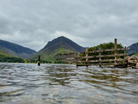 Weathered wooden fence partly submerged in calm lake water, with distant mountain rising in the background. - Powered by Adobe