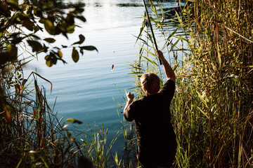 A mature woman fishing on a sunny day on a lake shore. A back view of a person fishing on a river...