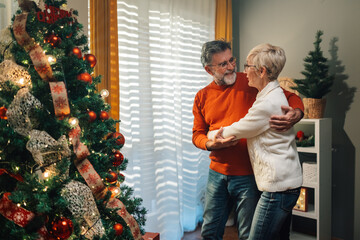 Senior couple dancing next to christmas tree at home