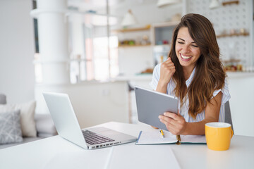 Fototapeta premium Young Woman Smiling While Using Tablet in a Bright Stylish Apartment for Work