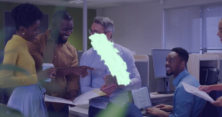 Five coworkers gathering in open-plan workspace, holding tablet and printed documents