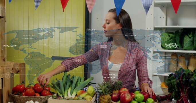 Female vendor in plaid shirt selecting red tomatoes at market stall, with produce and pennant flags