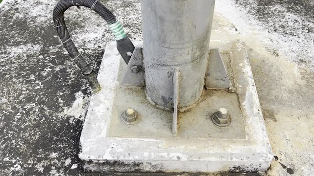 Foot of a weathered metal pole grounded to a concrete base on a patchy surface detailing construction anchoring maintenance and outdoor conditions