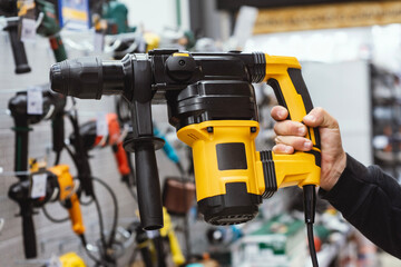 Close-up of a person holding a heavy-duty yellow electric rotary hammer drill in a hardware store....