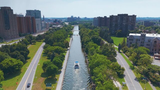 Aerial view of Ottawa's Rideau Canal with a boat navigating through the tree-lined waterway, surrounded by urban parkland and high-rise buildings.