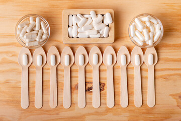 White vitamin pills in wooden box, wooden spoons and glass bowls with vitamins on wooden desk from above on wooden background. Minerals and food supplements to protect your health and immune system.