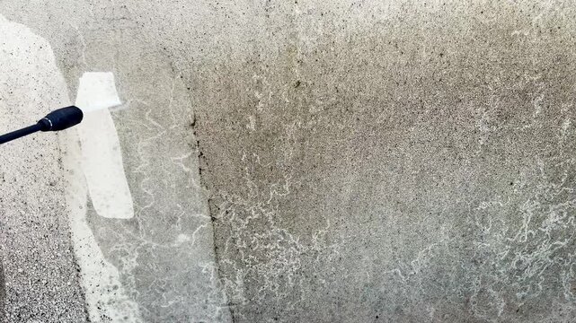 Pressure washing equipment being used to write the word Hi when cleaning dirt and grime off a wall