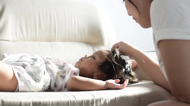 Adult comforting a sleepy child on the couch, hand fixing hair while toddler rests calmly at home