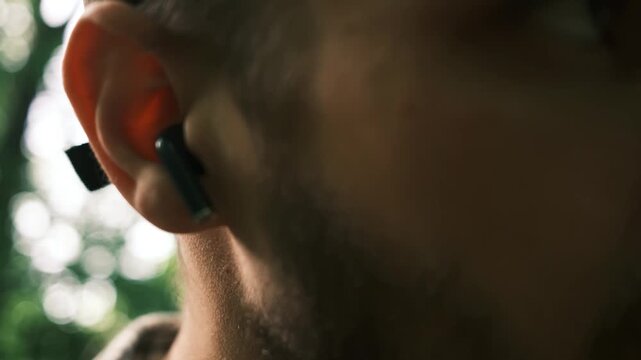 Close-up of a mans hands taking wireless earbuds out of a case in a forest park and putting them in ears to listen to music while walking. Horizontal 4k footage