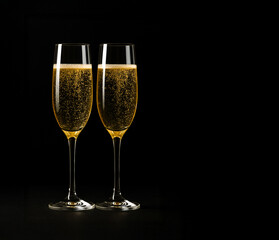 Close-up of two champagne flutes with golden sparkling wine and rising bubbles, side by side on a dark background