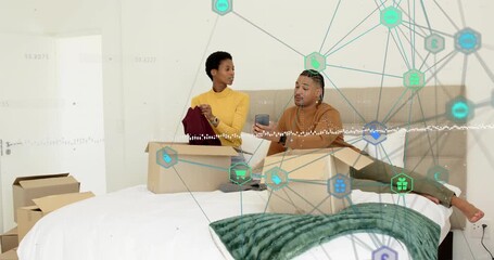 Woman unpacking clothes on bed as man taps phone generating graphics confirming online order status