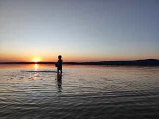 Fototapeta premium Silhouette of a Child Playing in Water at Sunset